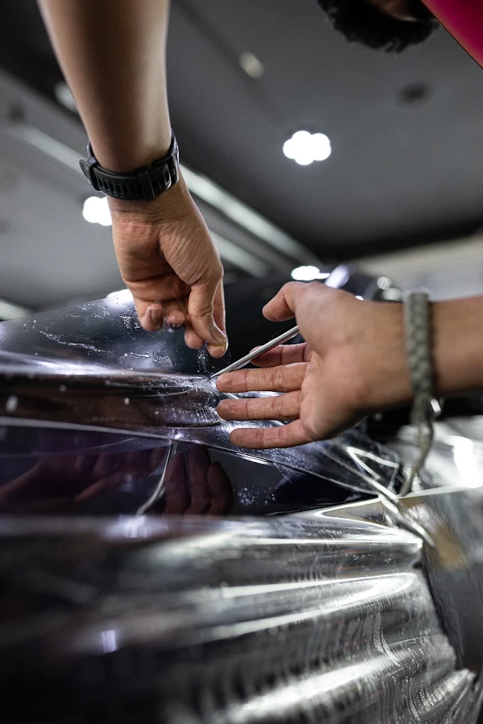 Installer applying clear paint protection film to a dark vehicle panel